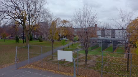 Drone-descending-on-a-public-park-with-a-batting-cage-and-a-basketball-court-on-a-grey-autumn-day