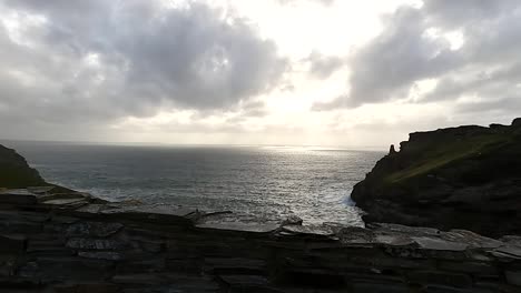 A-view-of-a-sunset-over-the-ocean-from-behind-a-rustic,-old-wall-ruin-at-King-Arthur's-Tintagel-Castle