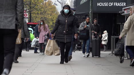 A-slow-motion-shot-of-people-with-shopping-bags-walking-along-Oxford-Street-as-the-new-Covid-regulation-three-tier-system-is-implemented,-allowing-non-essential-businesses-to-open-prior-to-Christmas