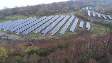 Solar-panel-array-rows-aerial-view-misty-autumn-woodland-countryside-push-in-left