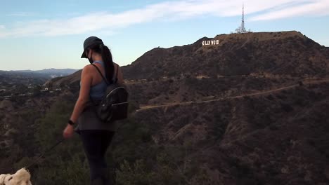 Healthy-female-wearing-pandemic-mask-hiking-with-dog-under-famous-landmark-Hollywood-sign