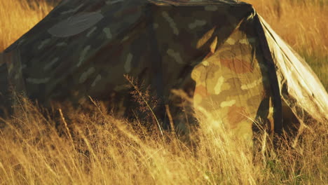 Camouflage-tent-in-grassy-field-with-front-flap-blowing-in-the-wind