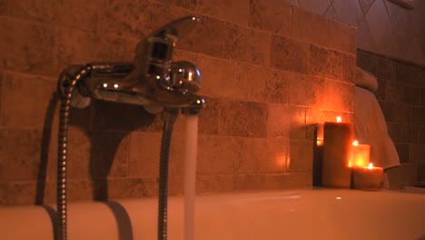 Hot-water-filling-up-a-home-spa-bathtub,-for-self-care,-with-candles
