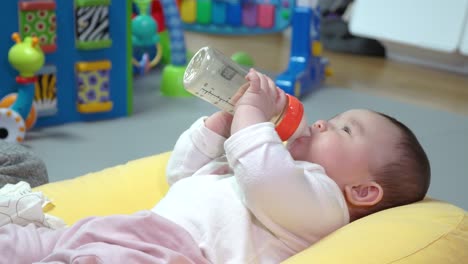 Süßes-Asiatisches-Baby,-Das-Milch-Aus-Der-Flasche-Trinkt-Und-Sich-Spielerisch-Auf-Und-Ab-Bewegt