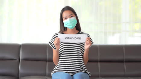 Mujer-Asiática-Con-Mascarilla-Que-Muestra-Un-Mensaje-Con-El-Hashtag-Stayhome-Durante-La-Pandemia-De-Covid-19,-Cuadro-Completo