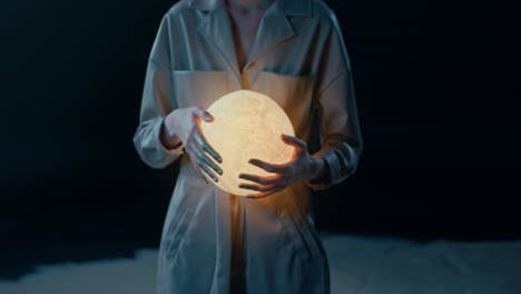 Unrecognizable-magician-holding-a-glowing-orb,-modern-artist-with-a-luminous-and-bright-sphere,-close-up