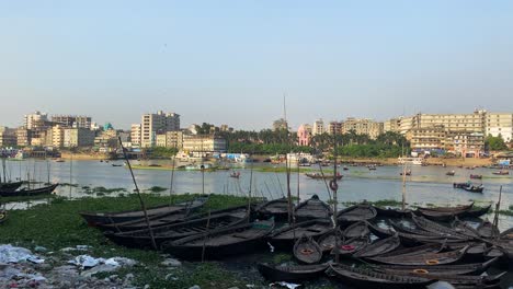 Buriganga-river-with-wooden-boats-wharf-and-city-view,-environment-pollution-concept
