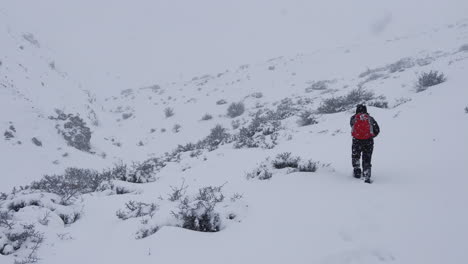A-man-with-a-red-backpack-walking-in-the-mountains,-in-a-snowstorm,-mountain-covered-full-of-snow