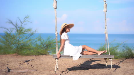 A-woman-sitting-on-a-large-wooden-swing-with-the-ocean-in-the-background-gently-rocks-back-and-forth