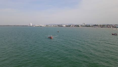 Umgekehrte-Luftaufnahmen-Dieses-Orangefarbenen-Fischerboots,-Die-Auch-Andere-Boote-In-Der-Nähe-Und-Die-Stadt-Pattaya-In-Thailand-Zeigen