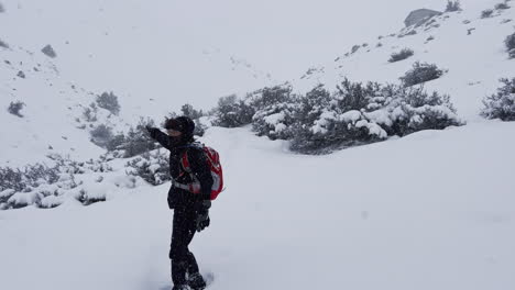 Back-view-of-a-man-hiking-in-the-mountains-in-winter,-covered-full-of-snow,-wearing-a-backpack