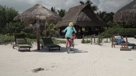 Mujer-Caucásica-Montando-Una-Bicicleta-En-La-Playa,-Usando-Una-Camisa-Azul-De-Protección-Solar