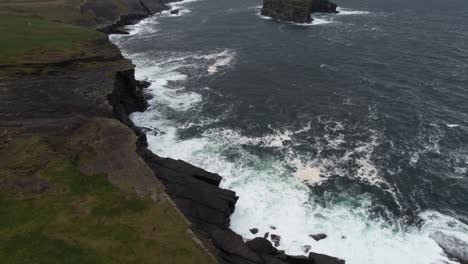 Aerial-View-of-Atlantic-Ocean-Waves-Breaking-Under-Cliffs-on-Irish-Coastline,-Tilt-Up-Revealing-Drone-Shot