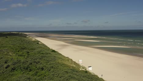 Aerial-shot-of-an-empty-beach-and-green-dunes-in-Oranjezon-nature-reserve-in-Zeeland,-the-Netherlands,-on-a-beautiful-sunny-morning
