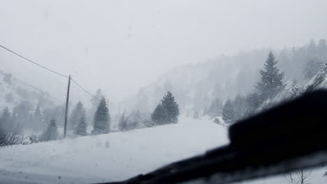 View-through-the-windshield-of-a-car-on-a-winter-road,-in-winter-along-which-the-car-is-driving-in-heavy-snow-and-wind