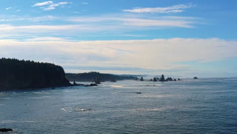 Stunning-aerial-drone-trucking-left-shot-of-the-gorgeous-Third-Beach-in-Forks,-Washington-with-large-rock-formations,-cliffs,-small-waves-and-sea-foam-on-a-warm-sunny-summer-morning