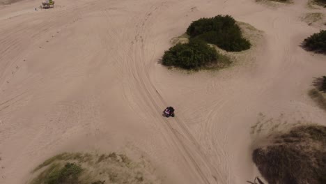 Aerial-moving-view-of-a-person-driving-a-quad-bike-on-the-beach-sand-in-a-forest-background-in-Mar-de-las-Pampas,-South-America