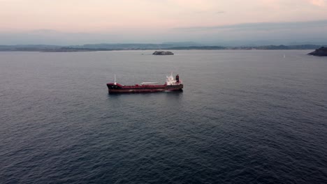 Industrial-tanker-vessel-near-coastline-of-Spain-with-remote-island-lighthouse,-aerial-view