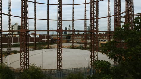 Drone-footage-of-Victorian-gas-holder-in-Bethnal-Green-with-London-city-skyline-in-background-on-cloudy-day