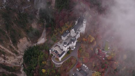 Neuschwanstein-castle-with-colorful-trees-during-autumn-season-on-cloudy-day,-aerial
