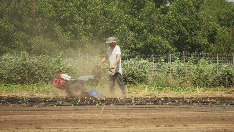 Young-farmer-boy-tilling-the-soil-with-engine-powered-tiller-on-organic-farm
