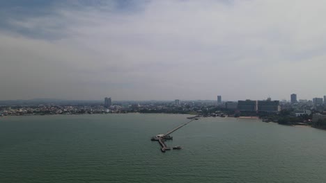 Imágenes-Aéreas-Hacia-Un-Muelle-Con-La-Playa-Y-La-Ciudad-De-Pattaya-En-El-Fondo,-Muelle-De-Pesca-De-Pattaya,-Pattaya,-Tailandia