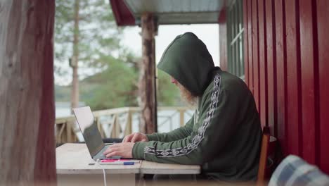 Young-Man-Hoodie-Working-On-Laptop-Computer-Outside-His-Cabin