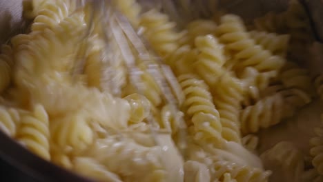 Close-up-View-of-a-Hand-Using-a-Whisk-Stirring-in-a-Metal-Bowl-Full-of-Fusilli-Pasta-and-a-Cream-Cheese-Dough---Steady-Shot