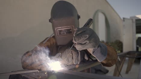 Person-with-protection-mask-is-welding-a-metal-object,-sparks-shooting