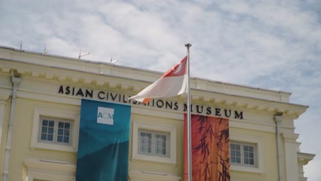 Singapore-Flag-Waving-In-The-Wind-In-Front-Of-The-Yellow-Facade-Of-The-Asian-Civilization-Museum-in-Singapore---Medium-Shot