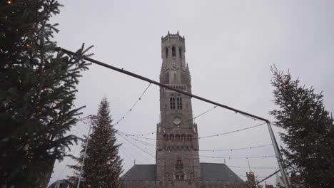 Low-wide-shot-of-Christmas-trees-and-belfry-on-the-market-square-in-Bruges,-Belgium