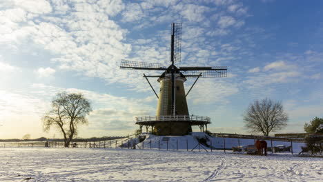 Time-lapse-of-clouds-passing-over-traditional-windmill-in-beautiful-white-winter-rural-landscape---zoom-in