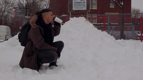 Young-man-kneeling-in-snow-taking-drink-of-hot-coffee