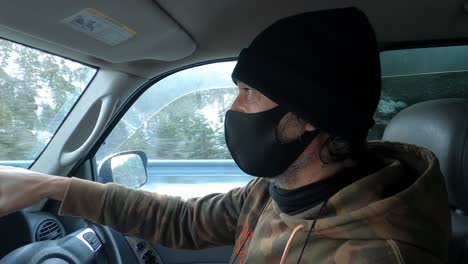 Interior-of-a-car-with-a-man-wearing-a-cloth-mask-as-he-drives-in-the-snow-during-the-COVID-19-pandemic