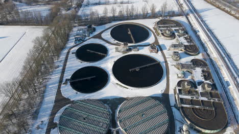 Aerial-of-basins-at-sewage-water-treatment-plant-in-winter---drone-flying-backwards