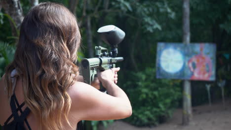 An-active-woman-with-a-paintball-gun-practices-shooting-at-a-target---concept:-frustration,-anger,-revenge,-relationship,-breakup,-ex-boyfriend