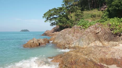 Rocks-and-beach-in-Thailand-with-bamboo-hut-on-hill-with-jungle,-ocean-and-Island