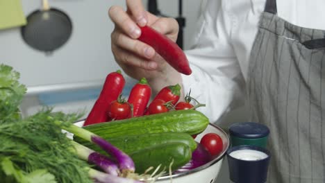 Chef-hand-picks-up-red-spicy-pepper-from-bowl-with-vegetables-on-a-kitchen-table