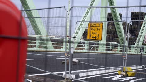 Covid-social-distancing-metal-sign-on-empty-closed-Runcorn-Jubilee-bridge-mesh-fence-left-dolly-fencing-closeup