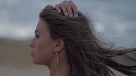 Dark-haired-women-with-a-wild-stare-wind-blowing-though-her-hair-in-an-scenic-cloudy-landscape-in-cinematic-slowmotion