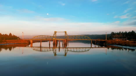 Drone-Flying-Over-Bullards-Bridge-With-Specular-Reflection-On-Coquille-River-During-Sunset-Near-Bandon-Marsh-National-Wildlife-Refuge-In-Oregon,-USA