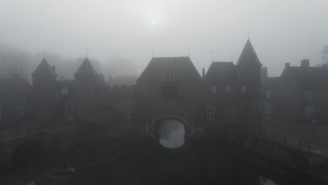 Jib-up-of-medieval-gate-over-river-with-thick-fog-in-the-background