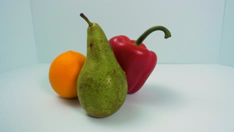 Frische-Große-Grüne-Birne,-Roter-Süßer-Paprika,-Saftige-Orange-Dreht-Sich-Langsam-Auf-Hellblauem-Hintergrund,-Gesundes-Lebensmittelkonzept,-Nahaufnahme,-Kamera-Dreht-Sich-Nach-Links