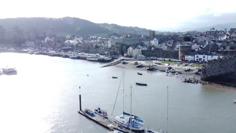 Idyllic-Conwy-castle-and-harbour-fishing-town-boats-on-coastal-waterfront-aerial-slow-rise-above-townscape