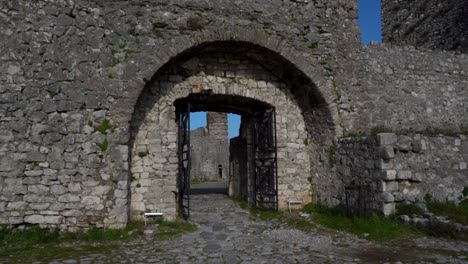 Entering-the-gate-of-ancient-fortress-with-stone-walls-and-cobblestones,-following-shot