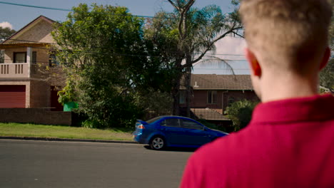 über-Die-Schulter-Eines-Weißen-Mannes-Mit-Rotem-T-Shirt,-Der-Auf-Ein-Pirschendes-Blaues-Auto-Blickt