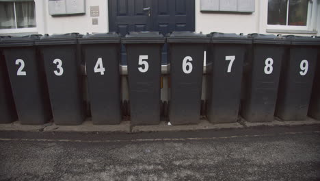 Numbered-rubbish-bins-lined-up-outside-apartment-complex,-slow-pan