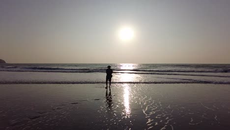 Early-Morning-Sunrise-Gimbal-Shot-Of-A-Man-In-Hat-Enjoying-Walking-On-Wet-Sandy-Beach---Slow-Motion