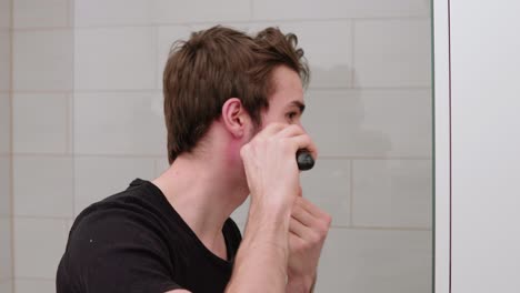young-man-trimming-and-shaving-his-own-beard-in-front-of-mirror-in-bathroom