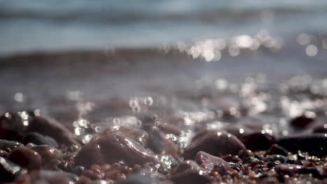 Water-washing-over-pebbles-on-sunny-beach,-close-up-shot